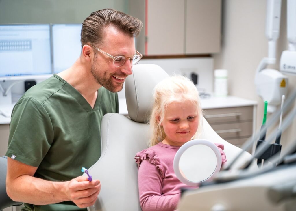 Tandarts laat een jong kind een spiegeltje zien in de behandelstoel